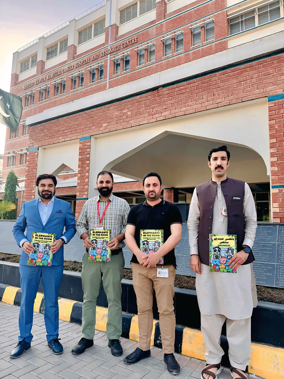 Four of the team holding copies of the comic outside Shaukat Khanum Memorial Cancer Hospital, Peshawar.