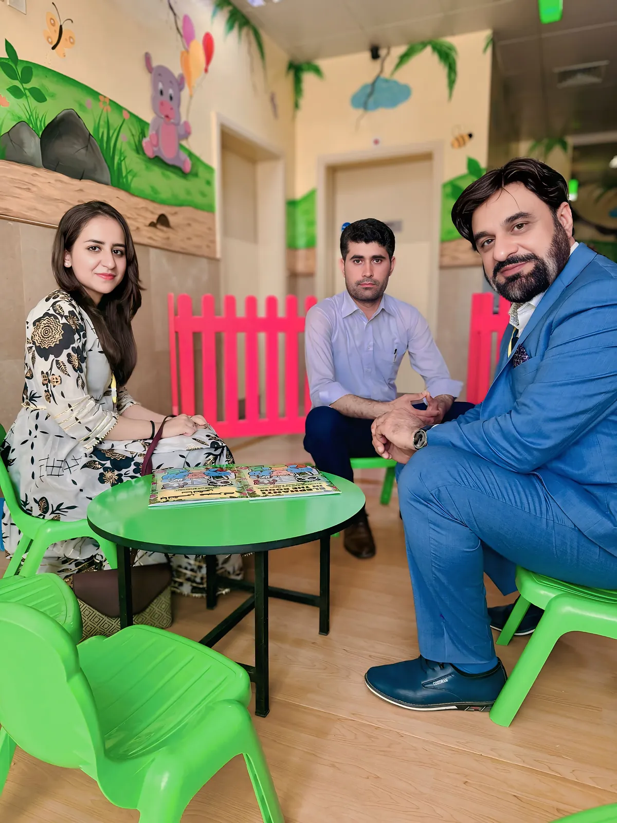 Dr Khan and a colleague sitting at a low table in the hospital play area, going through a comic with a young reader.
