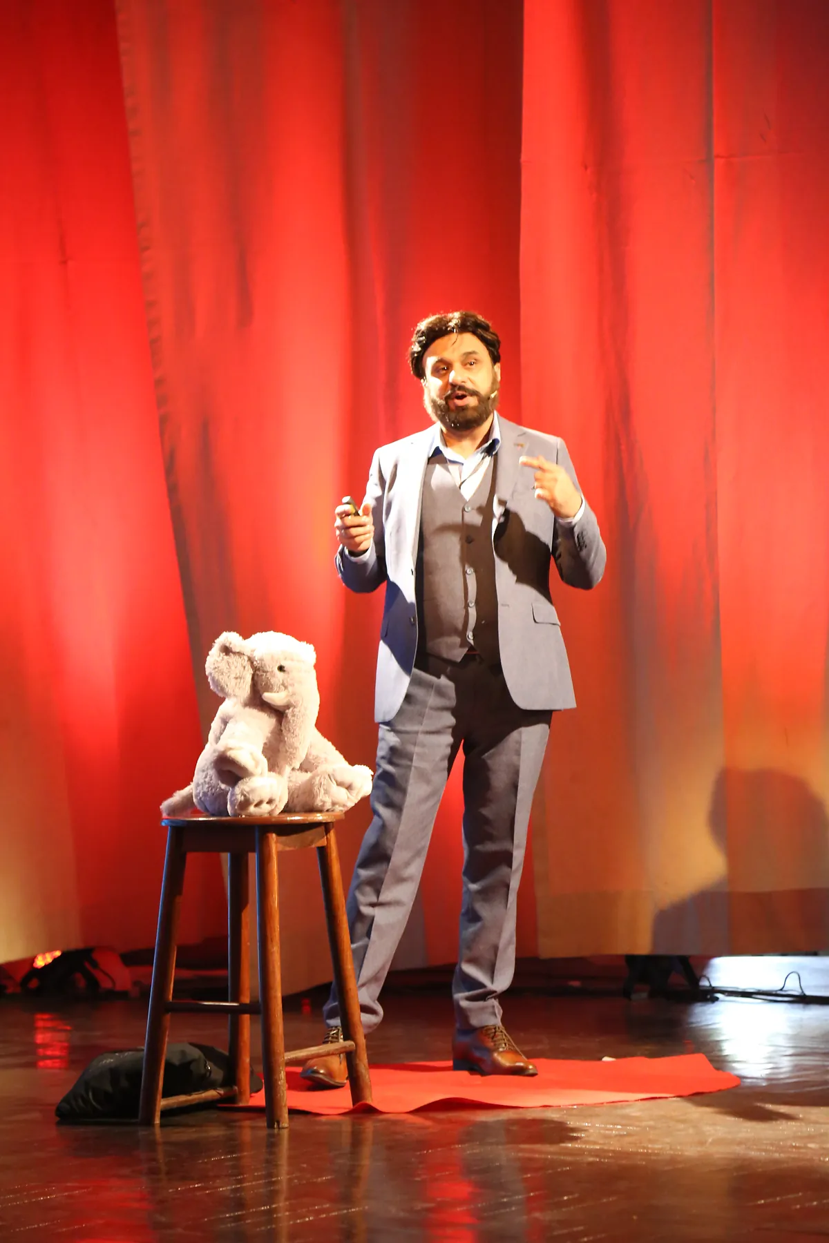 Dr Mohammad Muneeb Khan mid-talk on the TEDx stage, a plush elephant on a stool beside him.